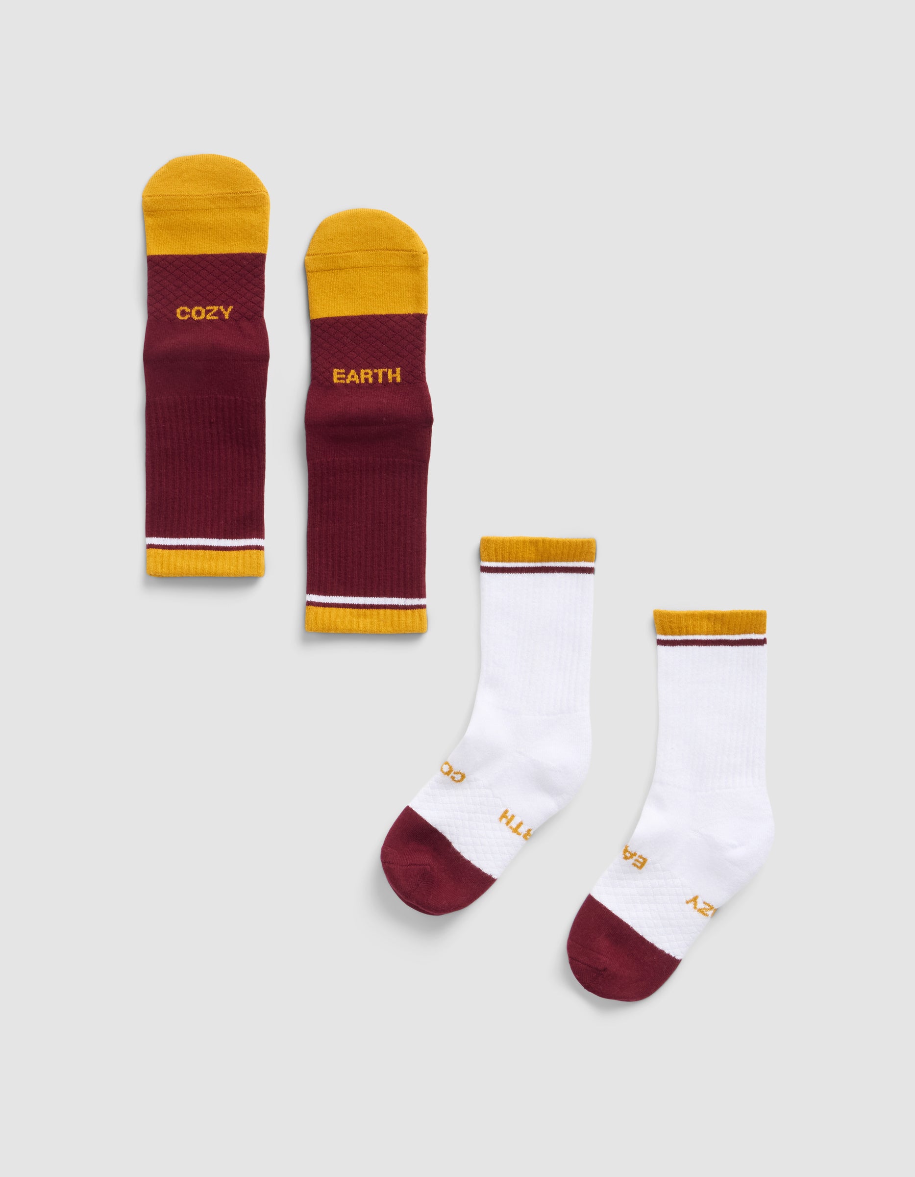 Four Cozy Earth Essential Calf Socks are shown: two burgundy and yellow with "COZY" and "EARTH" text, and two mostly white with burgundy toes, yellow/burgundy cuffs, and small "COZY EARTH" text, all on a light background.|Color:Burgundy
