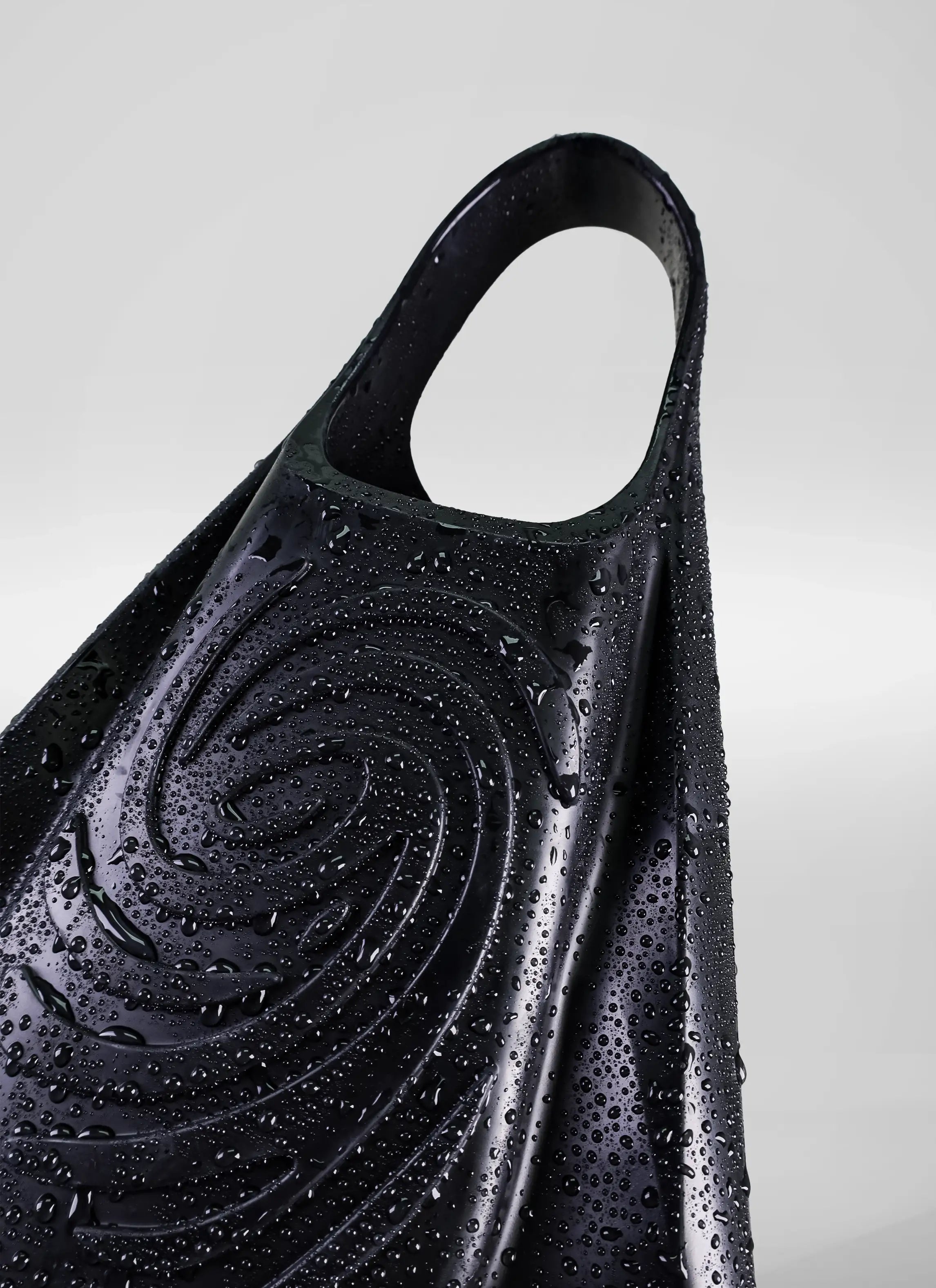 Close-up of a black bodyboard swim fin with water droplets and a spiral textured pattern.