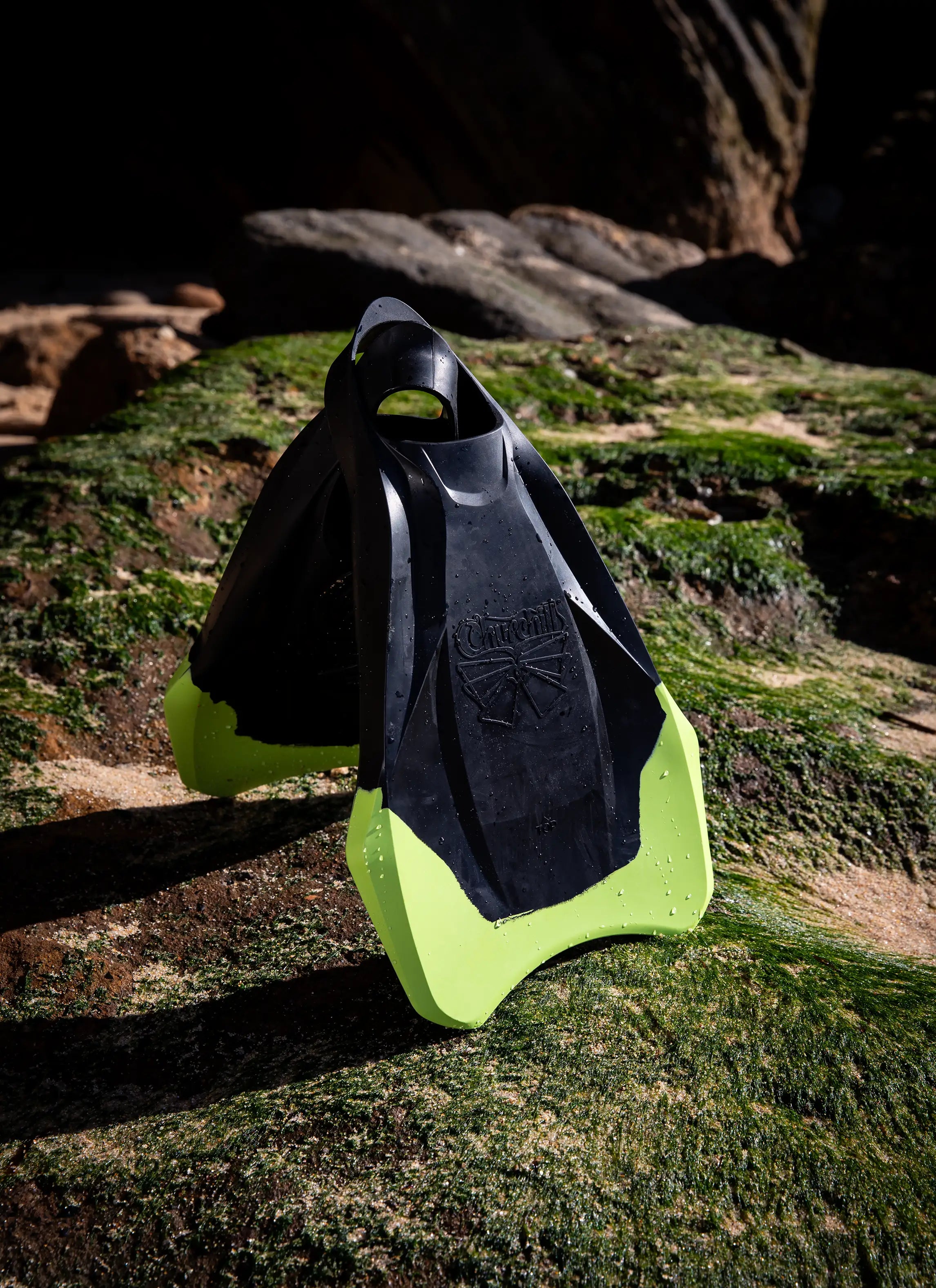 Black and yellow swim fins for bodyboarding on mossy rocks outdoors