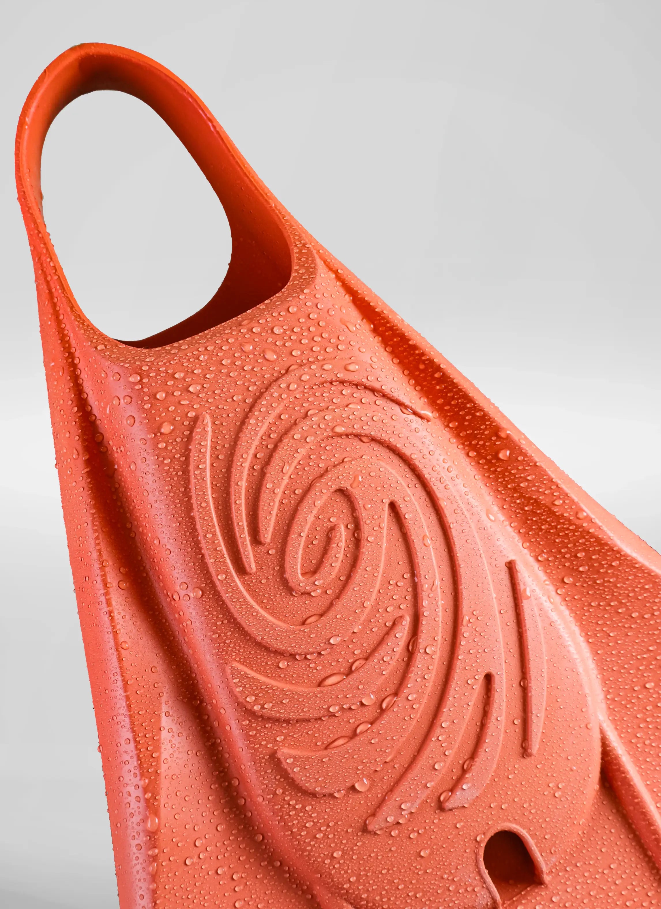 Close-up of a wet coral-colored bodyboarding swim fin with textured swirl pattern