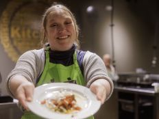 Woman in apron, holding a homecooked meal with vegetables.