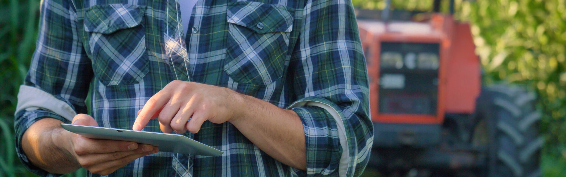 a person in a plaid shirt holding tablet, a red tractor in the background