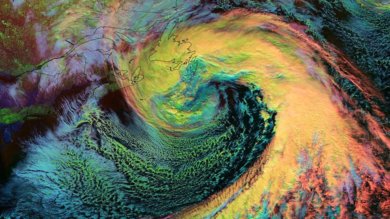 Enhanced satellite image from NOAA's Joint Polar Satellite System (JPSS) showing a massive nor'easter over the Atlantic Ocean on February 14, 2024. The storm appears as a dramatic spiral structure with vibrant false-color representation: bright yellow and orange areas in the center indicate thick, high-altitude ice clouds, while green and teal regions around the edges represent warmer cloud formations. The image displays the classic counterclockwise rotation of the storm system extending from eastern Canada southward toward the Caribbean. Thin black outlines show coastlines of North America. The visualization was captured by the VIIRS instrument, highlighting different cloud types and temperatures through color enhancement. This powerful storm system began in the Southwestern United States on February 10, eventually developing into a nor'easter that caused significant disruptions across the Mid-Atlantic and Northeast states.