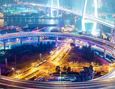 A bridge over water at night with city lights in the background.