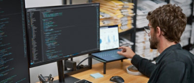 Una persona che usa un computer portatile a una scrivania e sullo sfondo uno scaffale di scatole.