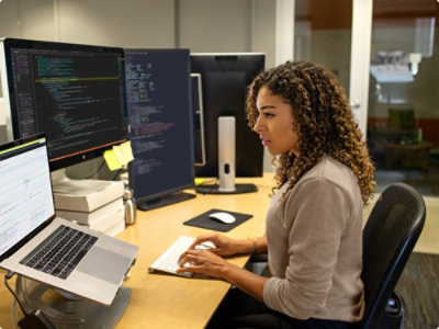 En person, der sidder ved et skrivebord og arbejder på en bærbar computer, der er placeret på et stativ.