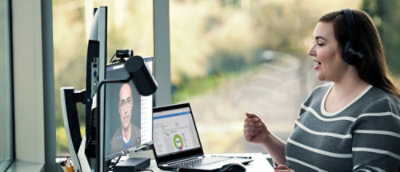 Person in einem Videoanruf am Schreibtisch mit Laptop und Monitor.