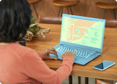 Eine Frau, die ein oranges Sweatshirt trägt und an einem aus Holz gefertigten Tisch einen Laptop nutzt, auf dem eine Website über Datensicherheit angezeigt wird
