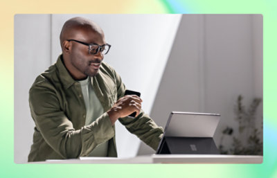 Uomo che tiene in mano una tazza di tè e guarda lo schermo di un portatile.