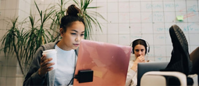 Dos personas trabajando con portátiles en una oficina moderna. Una persona sostiene una taza de café