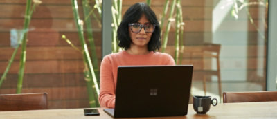A woman wearing glasses and a pink shirt sitting at a desk with a laptop.