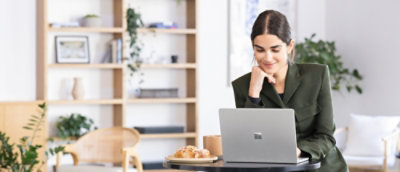 Orang duduk di meja bundar di kantor modern, bekerja di laptop dengan secangkir kopi dan kue di dekatnya.