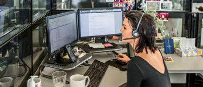 A woman wearing a headset and sitting at a desk with multiple computer screens.