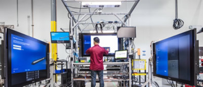 Tecnico che lavora su apparecchiature in un laboratorio high-tech circondato da monitor di grandi dimensioni.