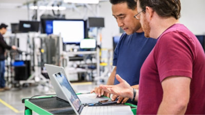 Two people reviewing information on a laptop in a factory setting.