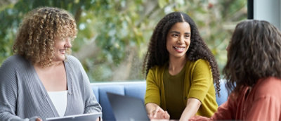 Three women talking with a laptop outdoors.