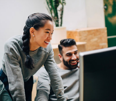 Une équipe collaborant à un poste de travail tout en passant en revue un contenu sur un grand moniteur de bureau dans un environnement de bureau.
