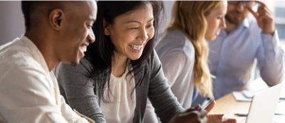 A diverse group of four people sitting at a table, smiling and looking at a laptop.