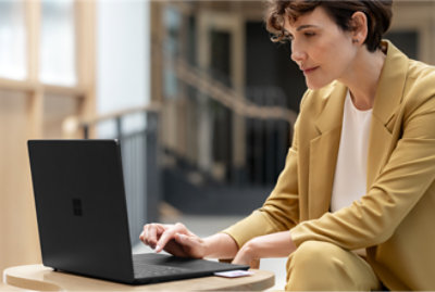 Uma mulher em um terno amarelo sentada à mesa usando um laptop.