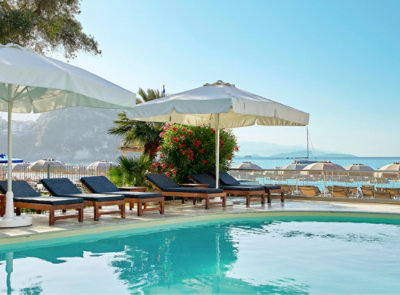 A white umbrella and lounge chairs by a pool with a blue surface.
