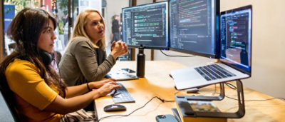 Eine Frau, die an einem Schreibtisch mit zwei Computerbildschirmen sitzt.