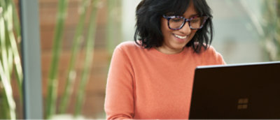 A woman in glasses smiling while using a laptop.