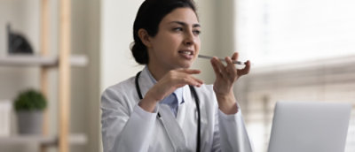 Un médico con bata blanca, con un estetoscopio, hablando por un smartphone mientras gesticula con la otra mano.