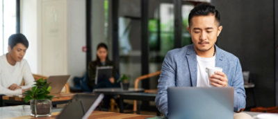 Seorang pria sedang memegang cangkir dan menggunakan laptop.