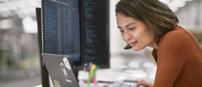 現代的なオフィス環境でコンピューターに向かい、コーディングに集中している女性。