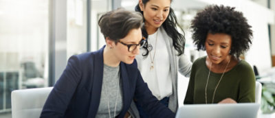 Tre donne che collaborano su un portatile in ufficio, impegnate in una discussione