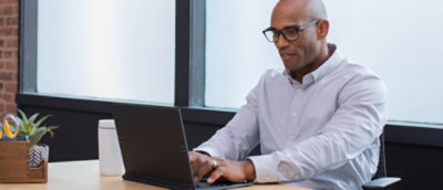 Person working on a laptop at a desk near a window in a modern office.