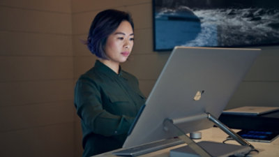 Une personne utilisant un ordinateur portable à son bureau, dans un espace de travail moderne équipé d’un écran.