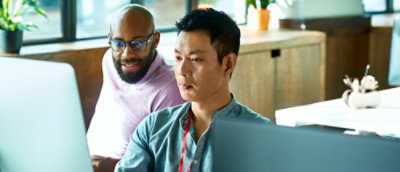 To kolleger sitter ved skrivebord, og konsentrerer seg om å arbeide på bærbare datamaskiner i et lyst kontormiljø.