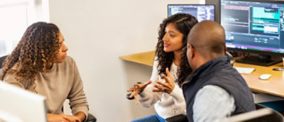  Three people reviewing information together near computer displays in an office environment.