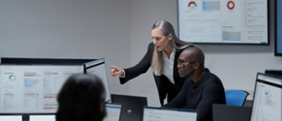 A woman pointing at a computer screen with a whiteboard in the background.