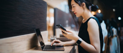A woman using both her laptop and her phone sitting on a table
