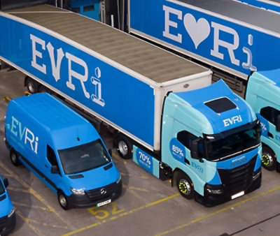 Sinisiä EVRi-jakelukuorma-autoja ja pakettiautoja pysäköitynä varikolle, ja kyljissä on suuret EVRi-merkinnät.