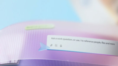 Imagem exibindo uma interface de chat com o prompt: "Faça uma pergunta de trabalho ou use / para referenciar pessoas, arquivos e mais"," em uma tela de fundo com gradiente