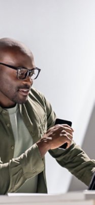 Person nutzt das Smartphone und arbeitet gleichzeitig am Laptop