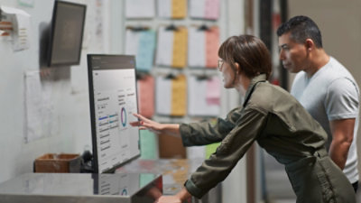 Deux personnes debout à l’intérieur examinent un tableau de bord sur un grand moniteur affichant des graphiques et des indicateurs.