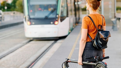 Una persona con una camiseta naranja y una botella negra de pie en una estación de tren.