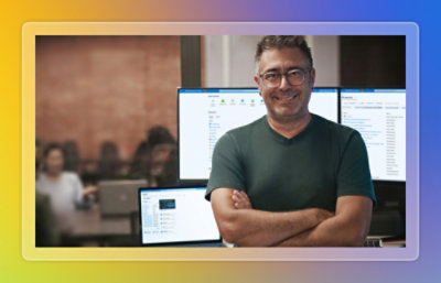 Hombre de pie con los brazos cruzados y sonriendo delante de varios monitores