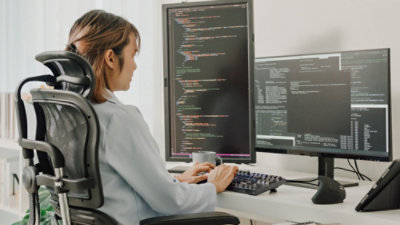 A person sitting at a desk working on a computer with text on the screen.