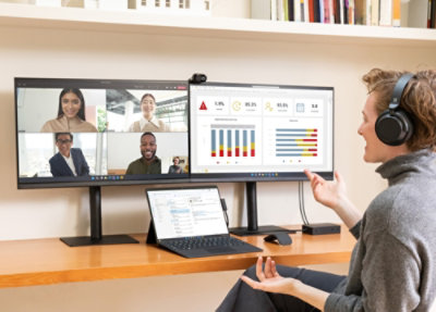 En person, der deltager i et videomøde på to skærme med analysedashboards.