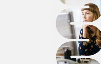 Nainen, joka katselee näyttöä työpöydän ääressä istuen.