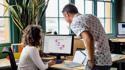Dwie osoby patrzące na monitor komputera z wyświetlonym diagramem w programie Visio.