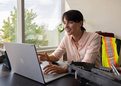 A woman wearing a pink shirt sitting at a desk using a laptop.