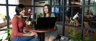 Two women sitting at a table with laptops.