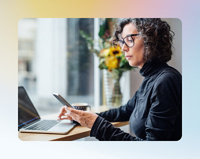 Uma mulher verificando algo em um celular com um laptop em uma mão