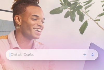 Nasmejan muškarac sedi i gleda u otvoreni laptop, sa uvećanom trakom za pretragu Copilot prikazanom pri dnu